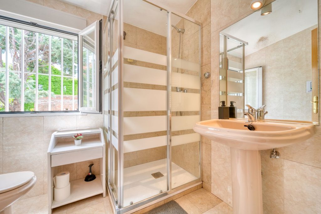 Lavabo en colonne dans une salle de bain habillée de marbre, à côté d'une cabine de douche