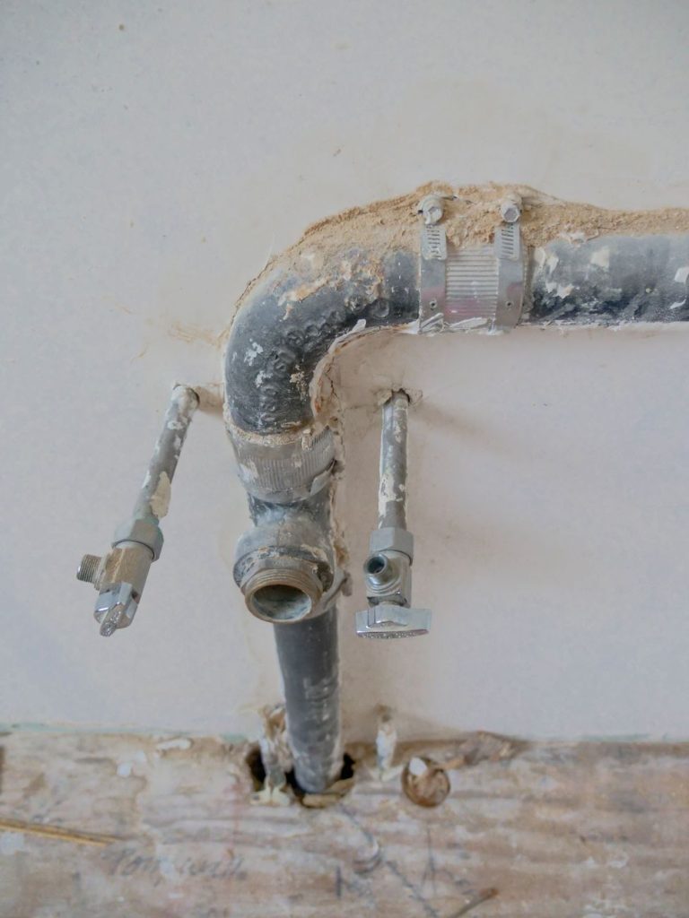 Anciennes arrivées d'eau et évacuation sortant d'un mur en cours de rénovation