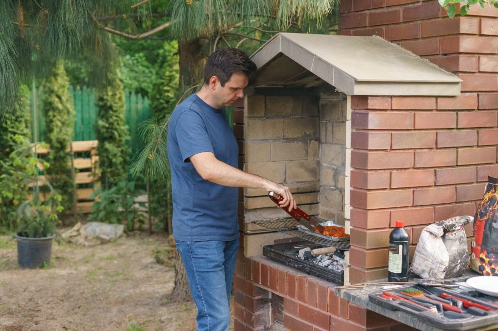 Homme cuisinant sur un barbecue fixe en briques dans un jardin