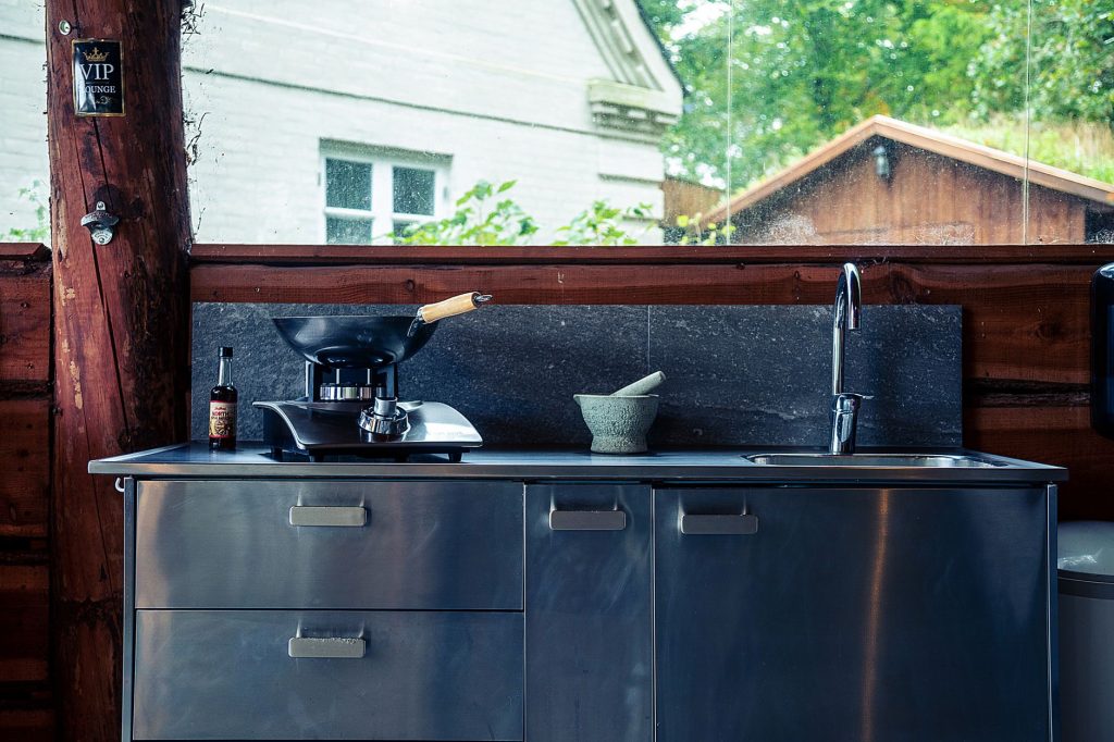 Cuisine d'été extérieure en inox avec évier et plan de cuisson sous un abri en bois