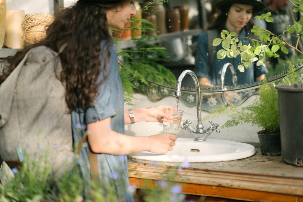 Personne remplissant un verre au robinet d'un évier extérieur entouré de plantes