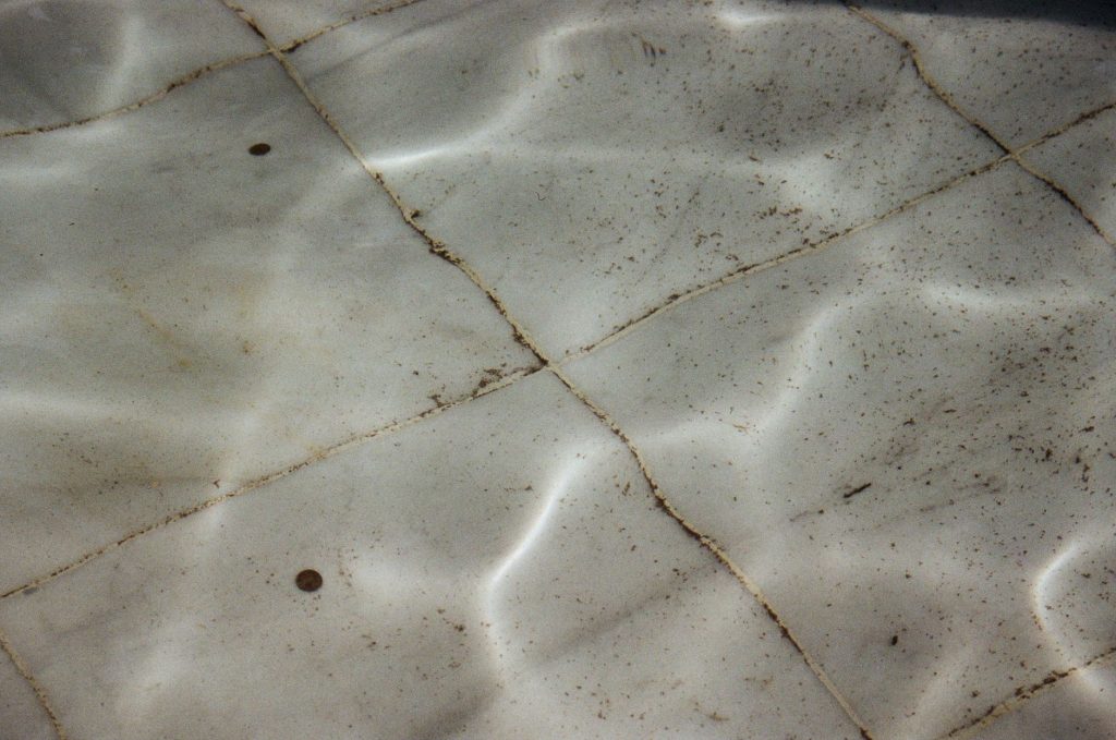 Fond de piscine carrelé couvert de petits dépôts et de débris
