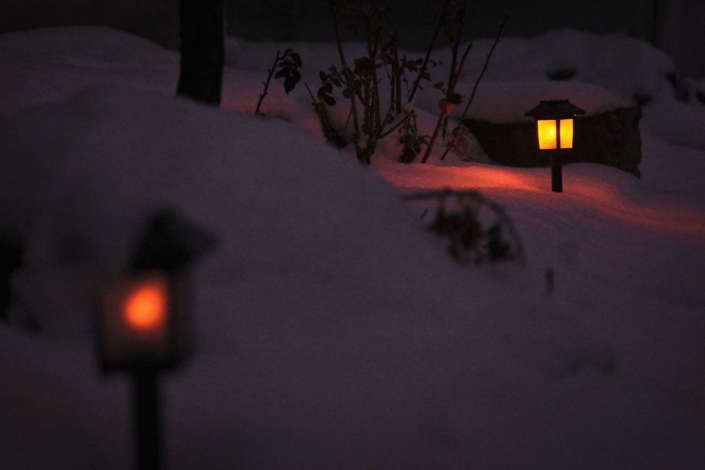 Lanternes de jardin allumées dans la neige à la nuit tombée
