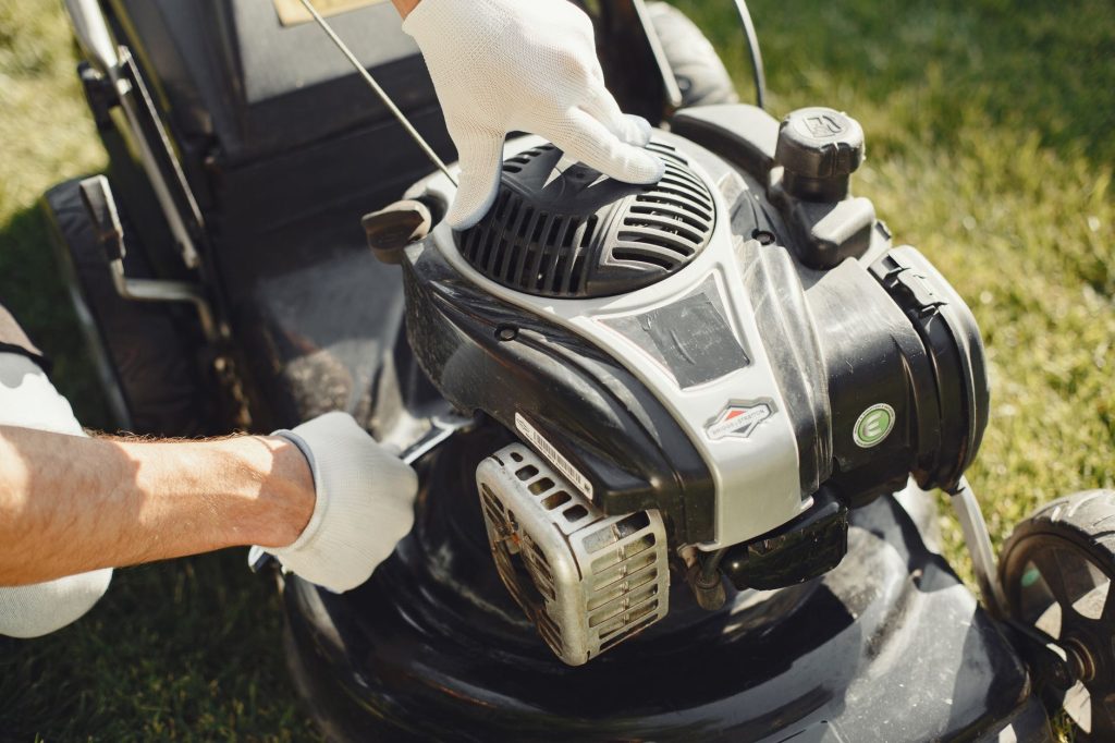 Mains gantées intervenant sur le moteur thermique d'une tondeuse