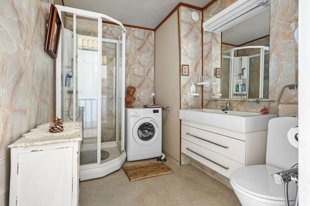 Petite salle de bain avec cabine de douche, lave-linge, meuble vasque et WC