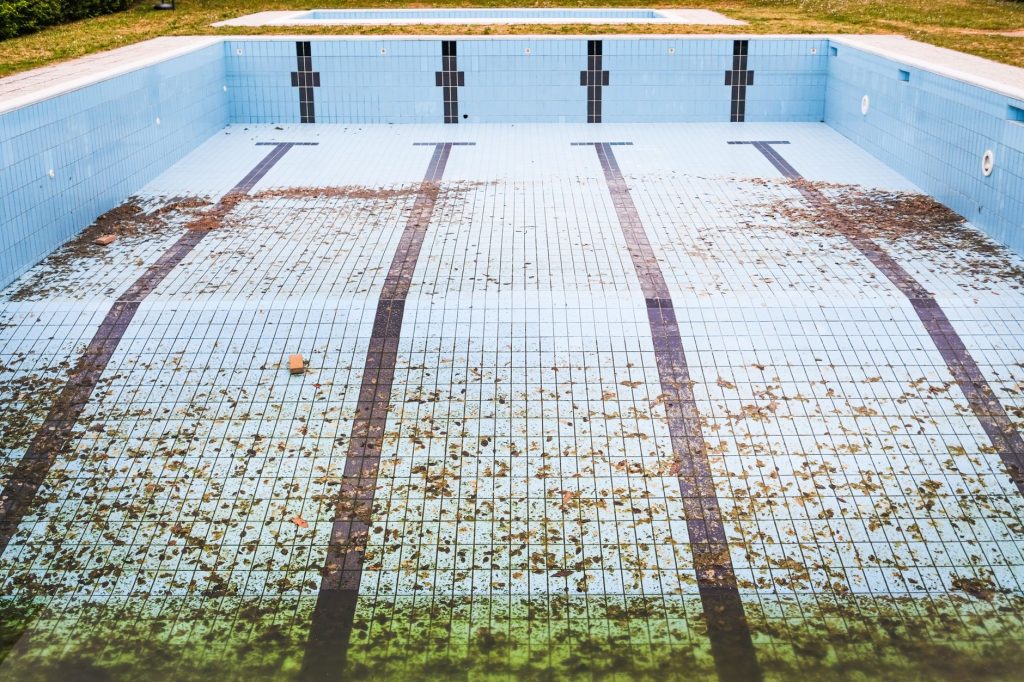 Piscine vidée dont le fond carrelé est couvert de feuilles mortes et d'algues