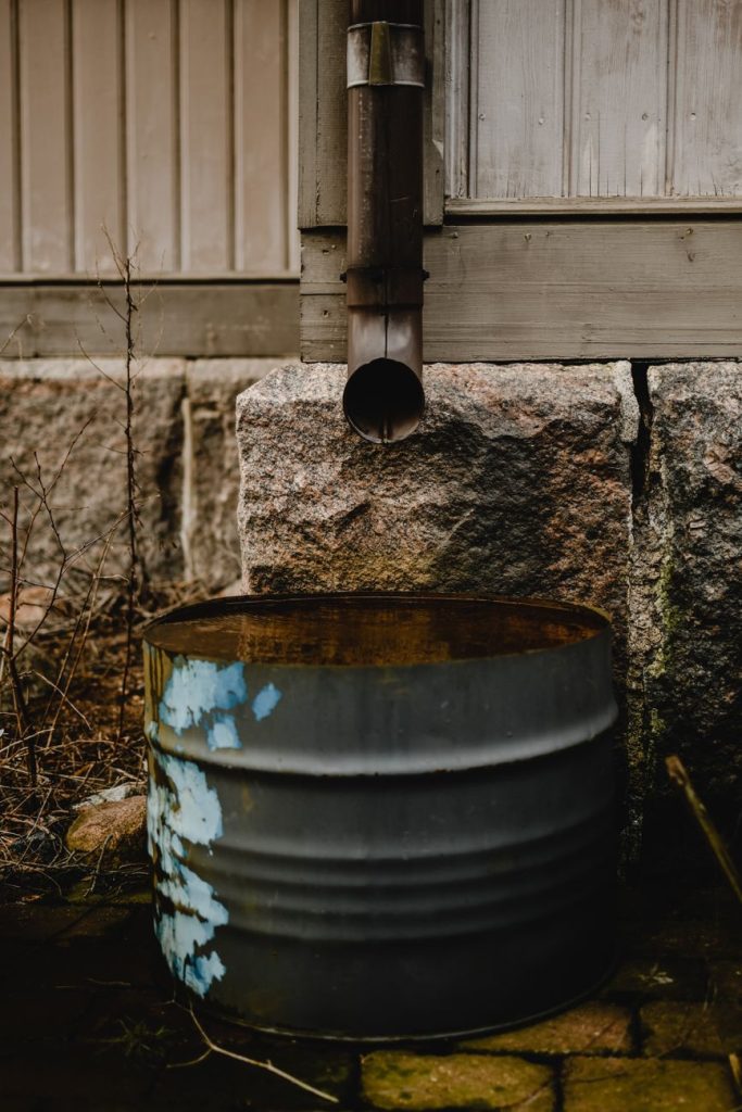 Tonneau métallique placé sous une descente de gouttière pour recueillir l'eau de pluie