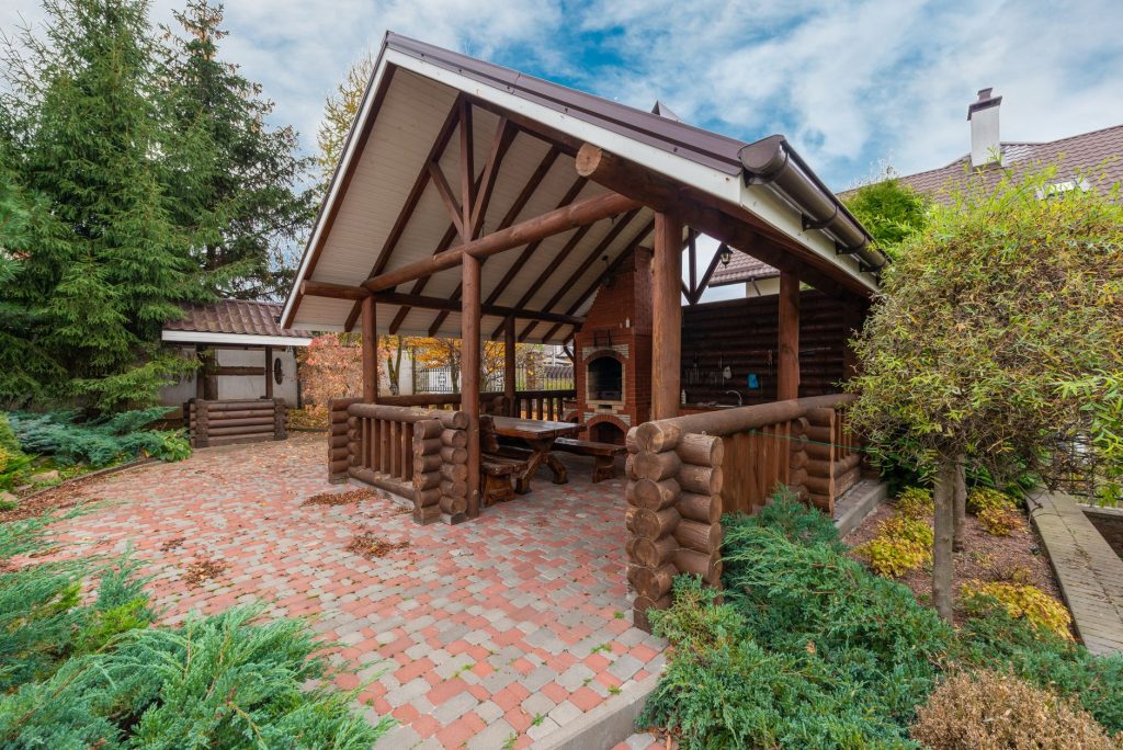 Abri de jardin ouvert en rondins de bois abritant une table et un barbecue maçonné