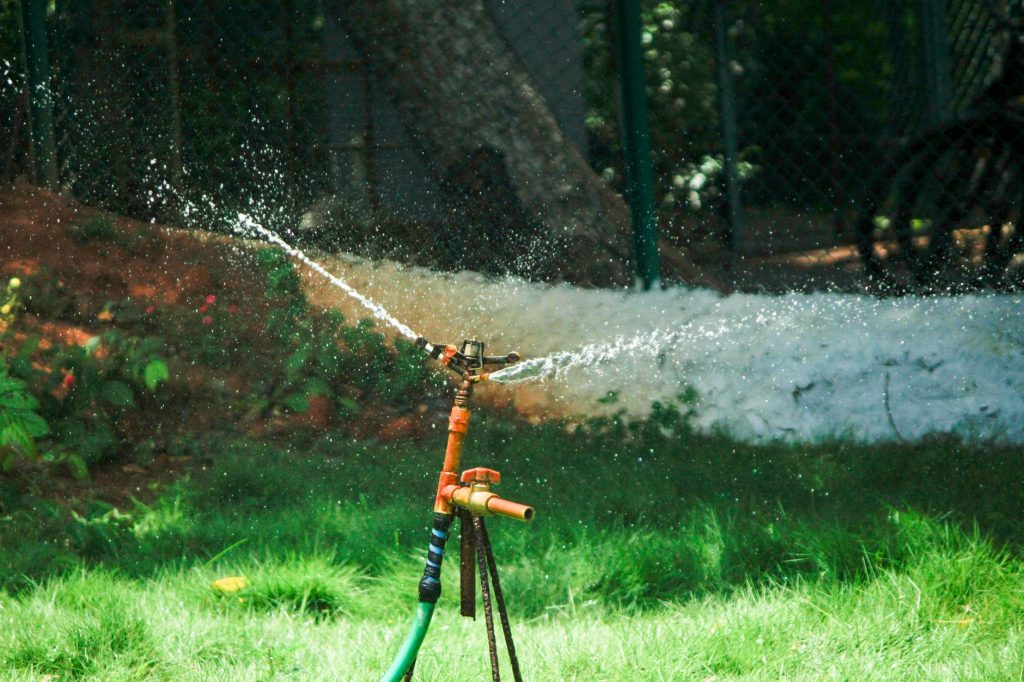 Arroseur rotatif sur trépied projetant de l'eau sur une pelouse
