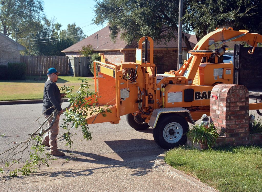 Professionnel introduisant des branches dans un broyeur tracté garé dans une rue résidentielle