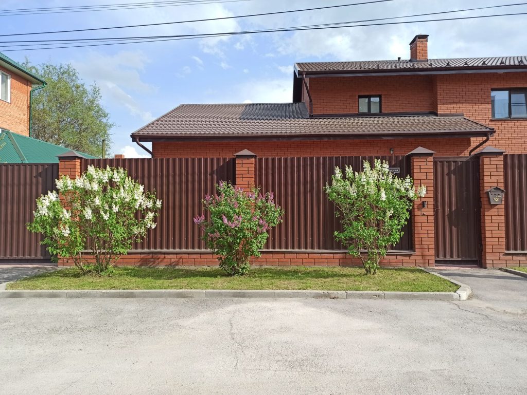Maison en brique entourée d'une clôture pleine avec portail et piliers maçonnés