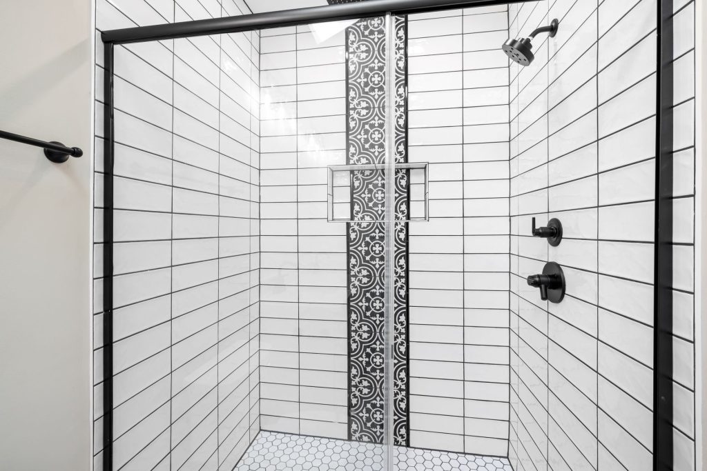 Douche carrelée de carreaux métro blancs posés à l'horizontale avec frise de carreaux à motifs et robinetterie noire