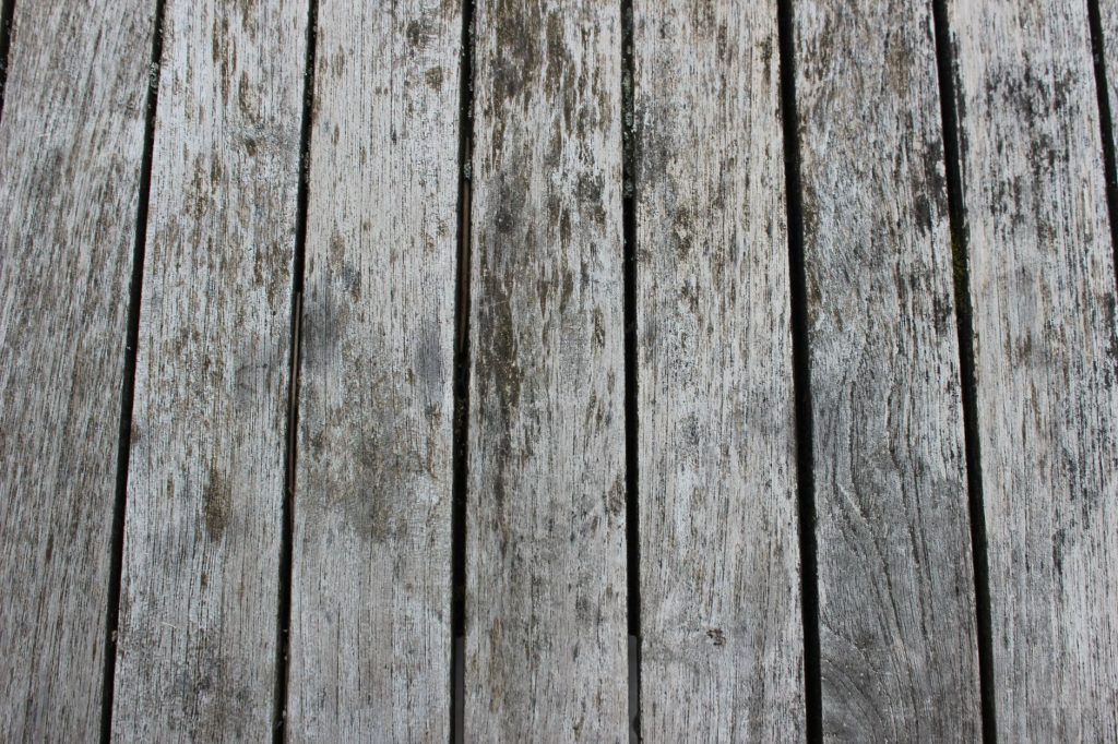 Lames de terrasse en bois grisées par le soleil et les intempéries, avec des traces sombres d'humidité