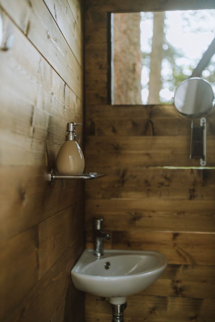 Petit lave-mains d'angle blanc fixé dans le coin de toilettes aux murs habillés de bois
