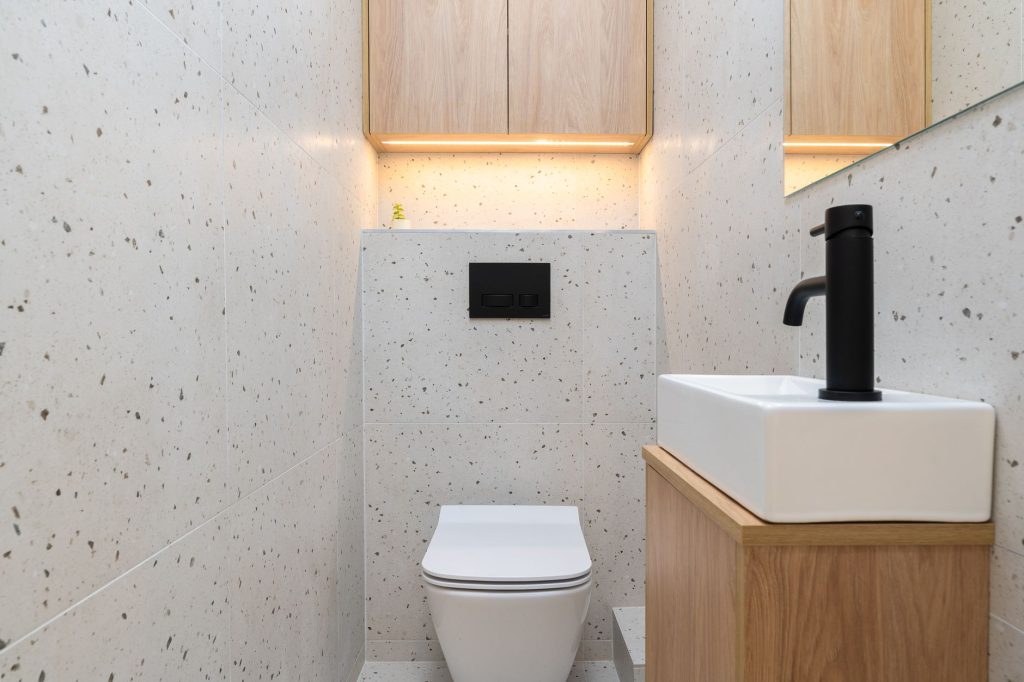Toilettes avec WC suspendu et lave-mains blanc posé sur un petit meuble en bois, robinet noir