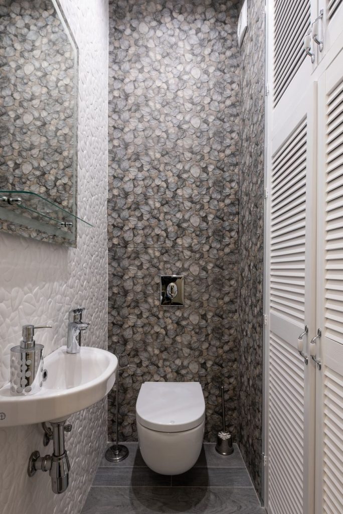 Toilettes étroites avec WC suspendu et petit lave-mains mural devant un mur de mosaïque