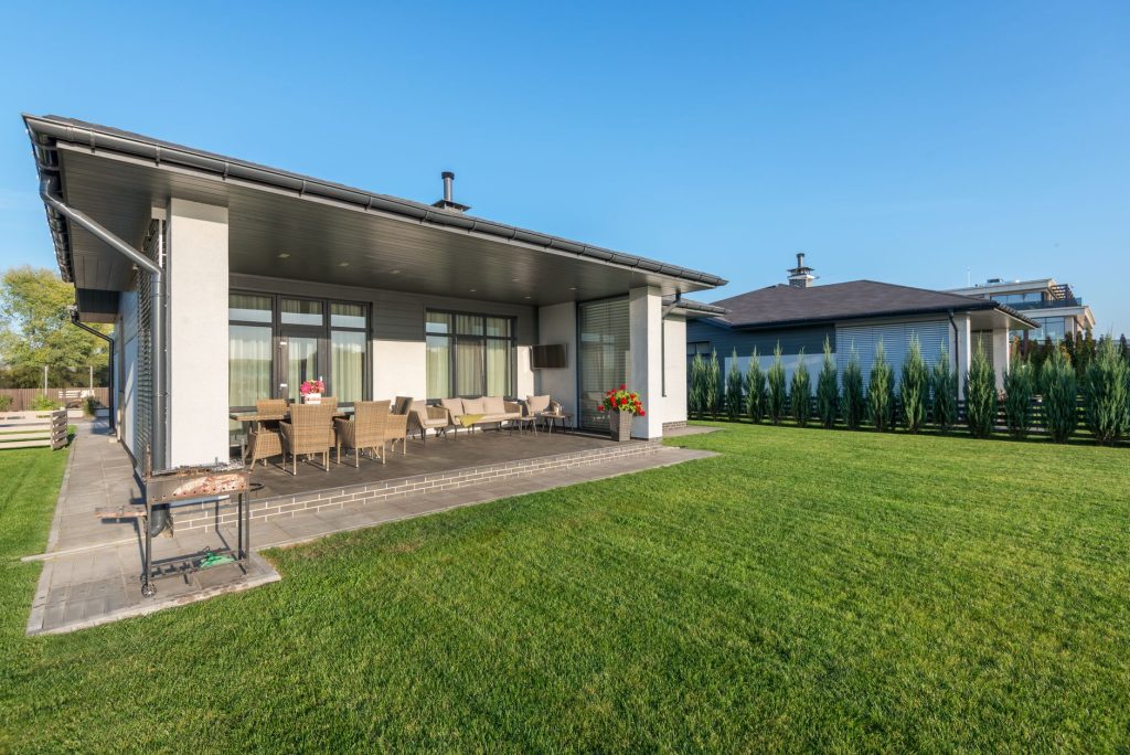 Maison contemporaine avec une grande pelouse verte et dense devant une terrasse couverte