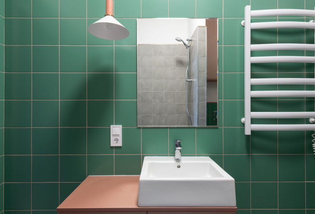 Mur de salle de bain carrelé en carreaux carrés verts avec lavabo, miroir et sèche-serviette blanc