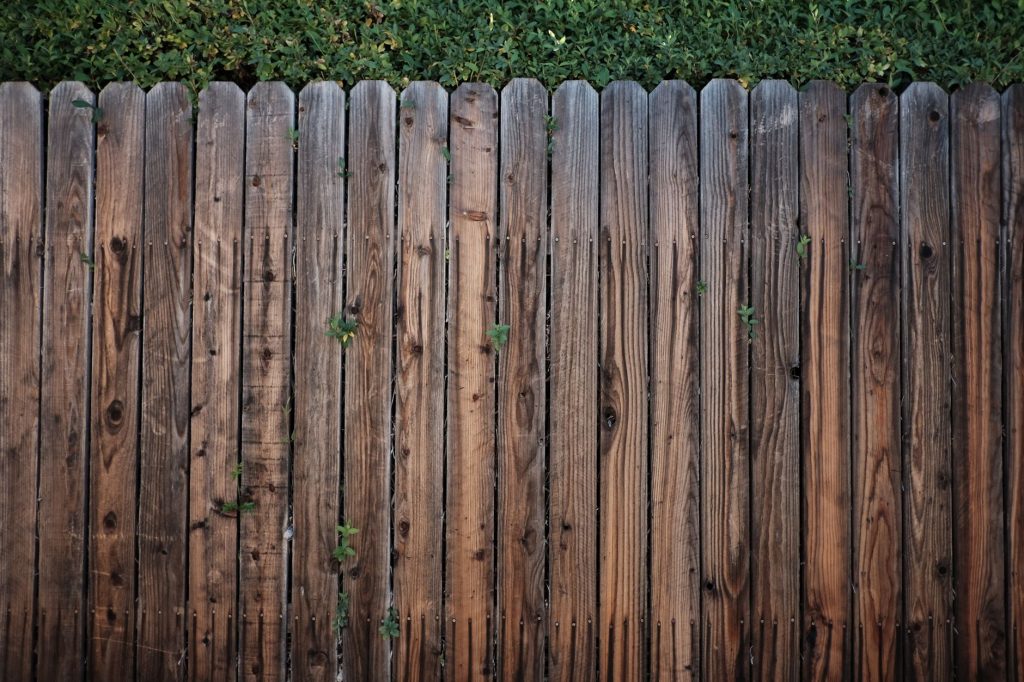 Palissade en planches de bois verticales jointives surmontée d'une haie