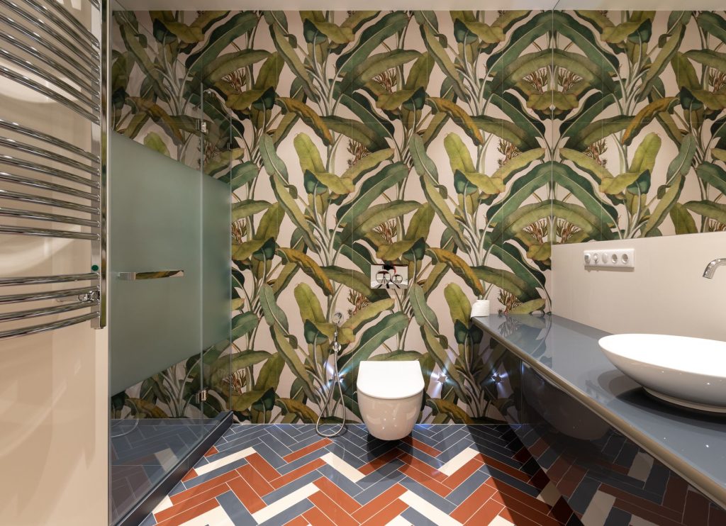 Mur de salle de bain habillé d'un papier peint à grands motifs de feuillages tropicaux derrière un WC suspendu