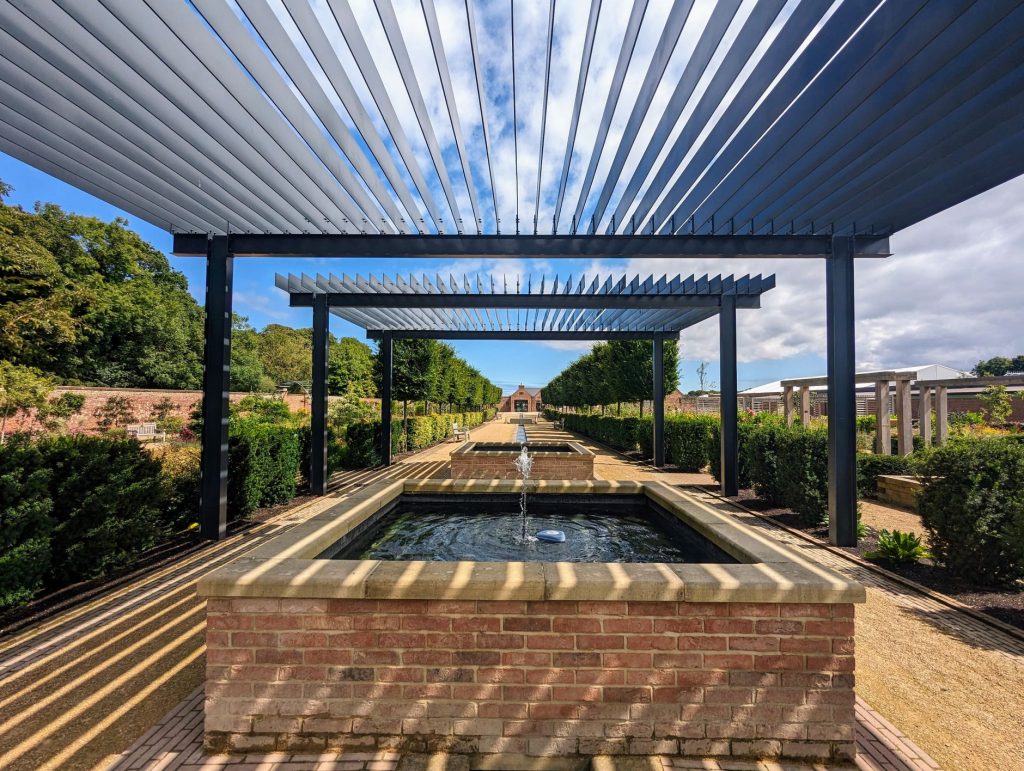 Pergola à lames orientables en aluminium vue de dessous, au-dessus d'un bassin de jardin