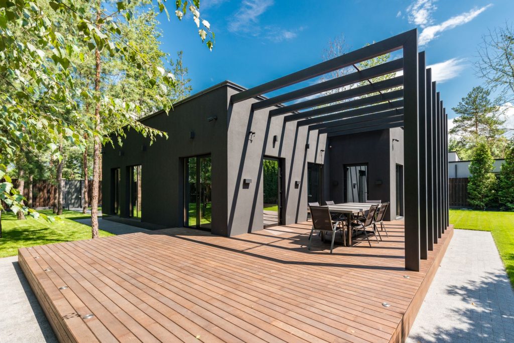 Pergola à poutres noires au-dessus d'une terrasse en bois devant une maison contemporaine