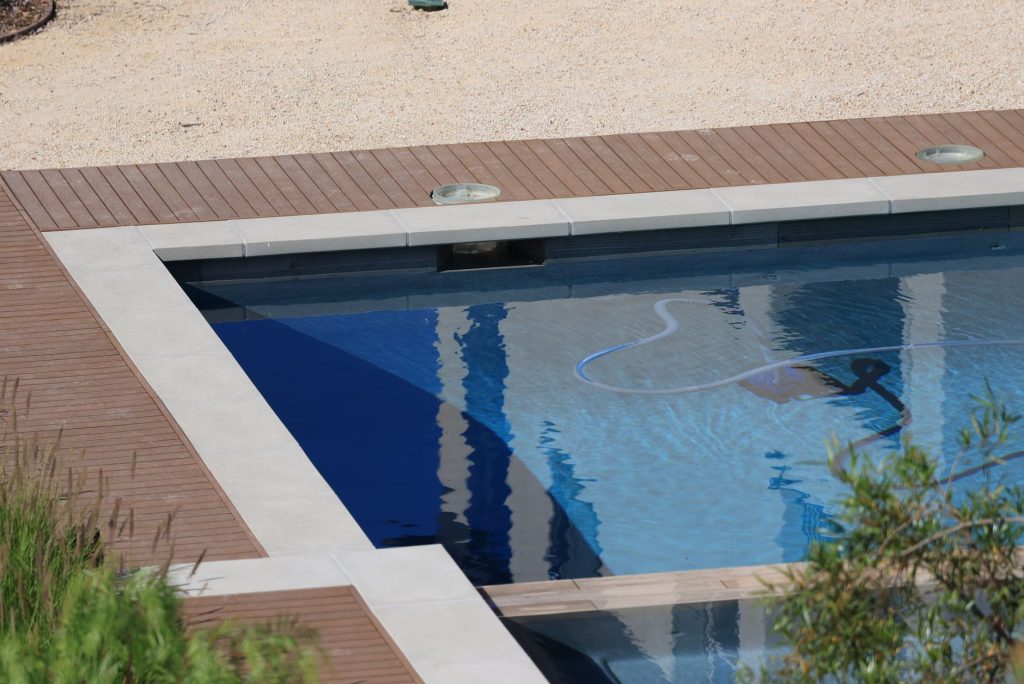 Plage de piscine en bois exotique brun autour d'un bassin enterré dans un jardin