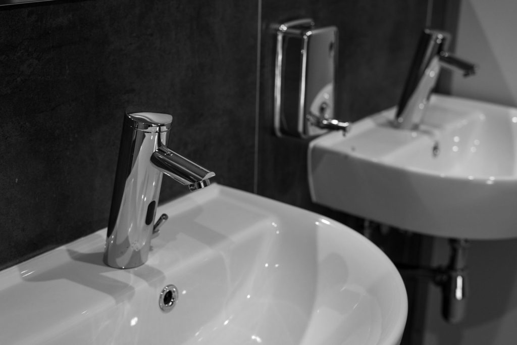 Robinet automatique chromé au-dessus d'un petit lavabo blanc fixé au mur
