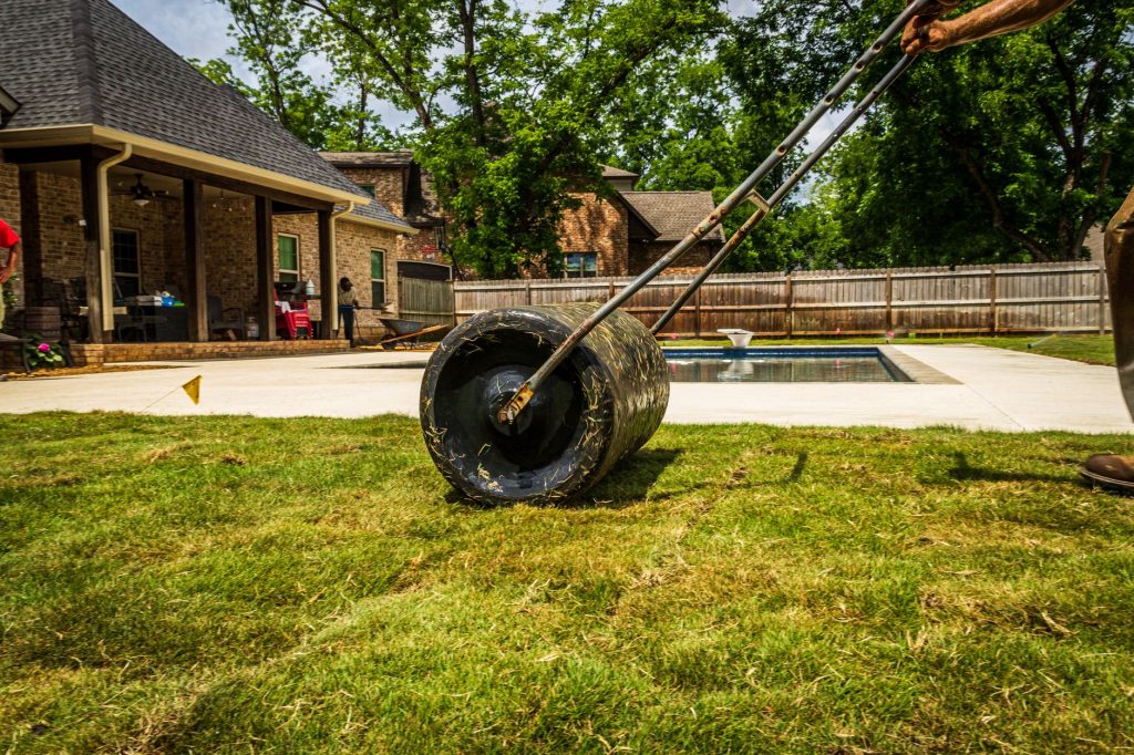 Rouleau à gazon passé sur une pelouse fraîchement posée près d'une terrasse et d'une piscine