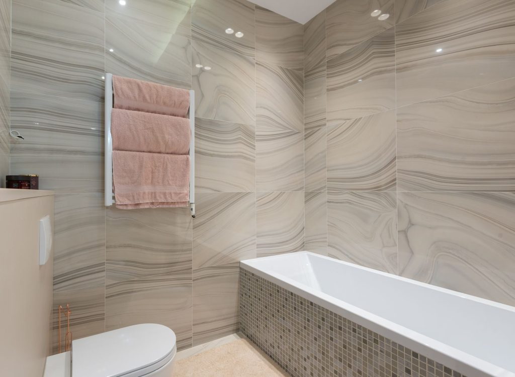 Salle de bain aux murs habillés de grands carreaux beiges veinés autour d'une baignoire encastrée