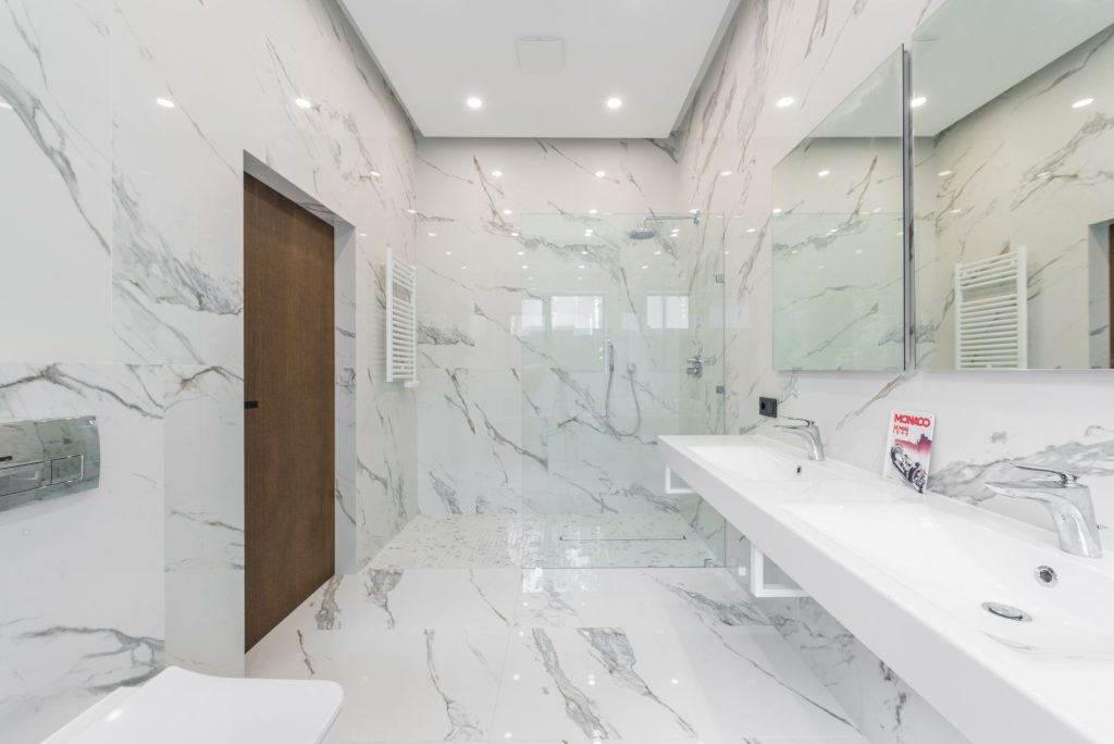 Salle de bain habillée de grandes plaques effet marbre blanc sur les murs et le sol, avec douche vitrée et double vasque