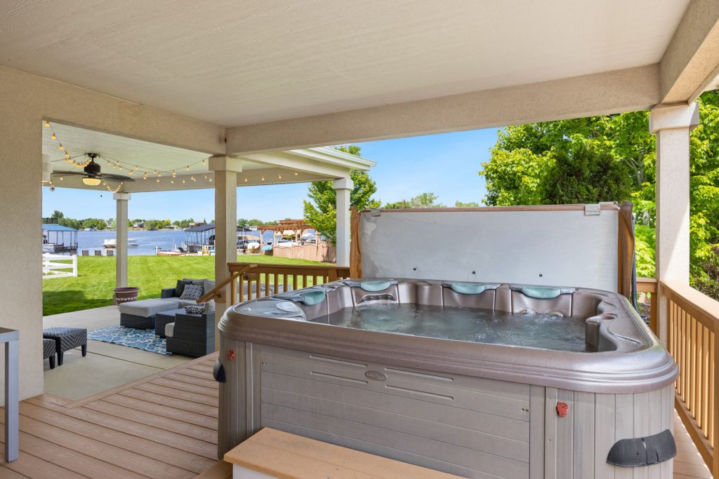 Spa rigide installé sur une terrasse couverte en bois, couverture relevée, face au jardin