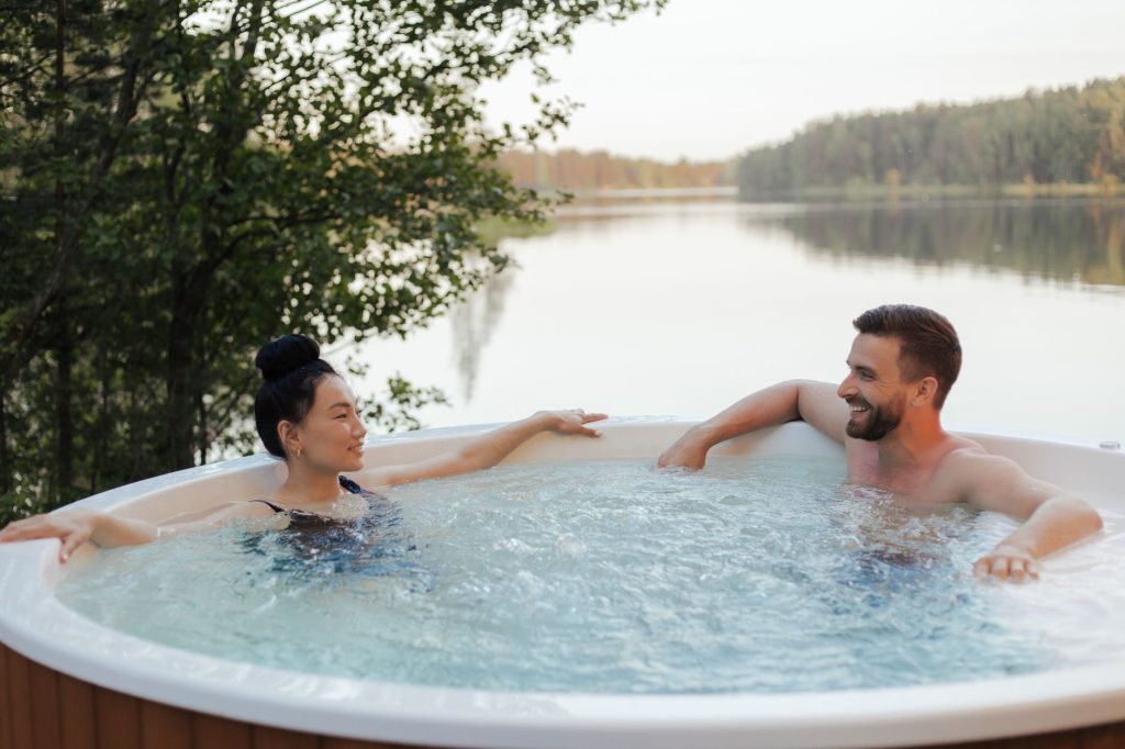 Deux personnes se détendant dans un spa rond en bois au bord d'un lac