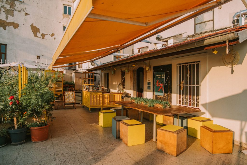 Grand store banne orange déployé depuis une façade au-dessus d'une terrasse aménagée avec table et assises