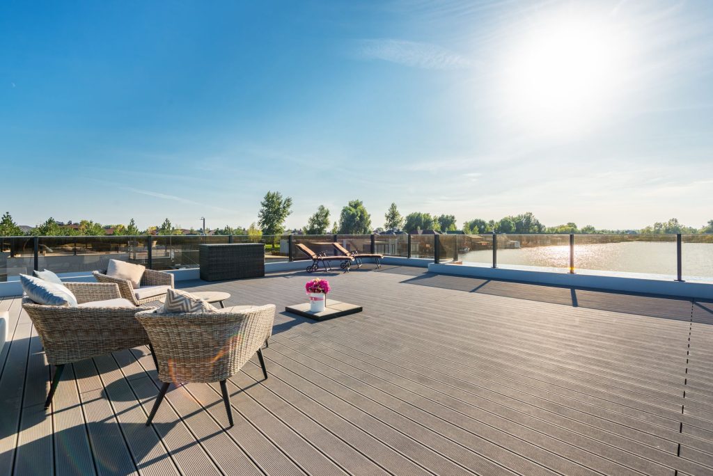 Grande terrasse en lames avec salon de jardin et transats au bord d'un lac sous le soleil