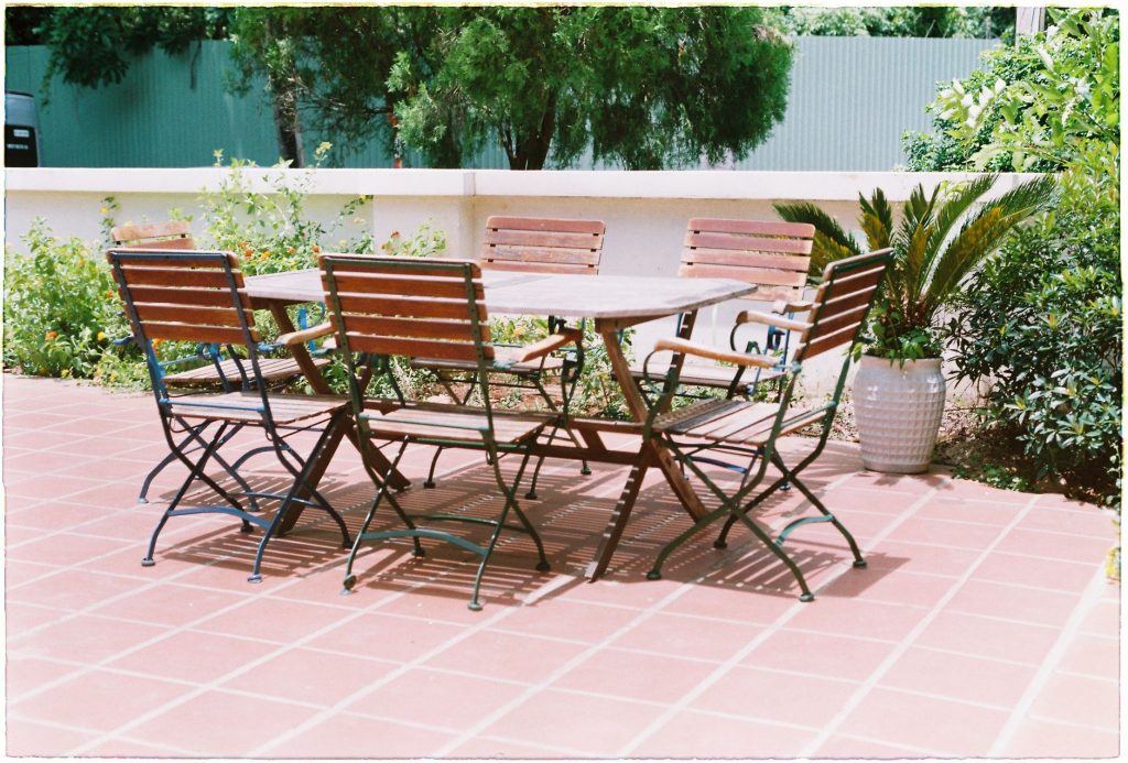 Terrasse en carreaux de terre cuite avec table et chaises de jardin en bois devant des massifs